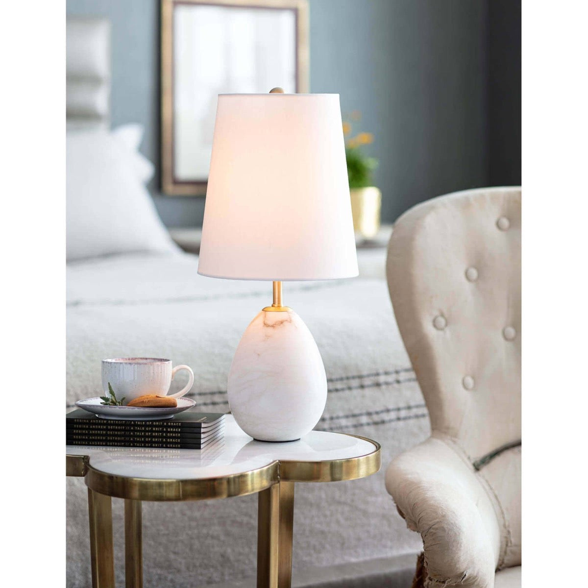 Isaac Alabaster Mini Lamp styled on a marble coffee table in a bedroom. Styled view.