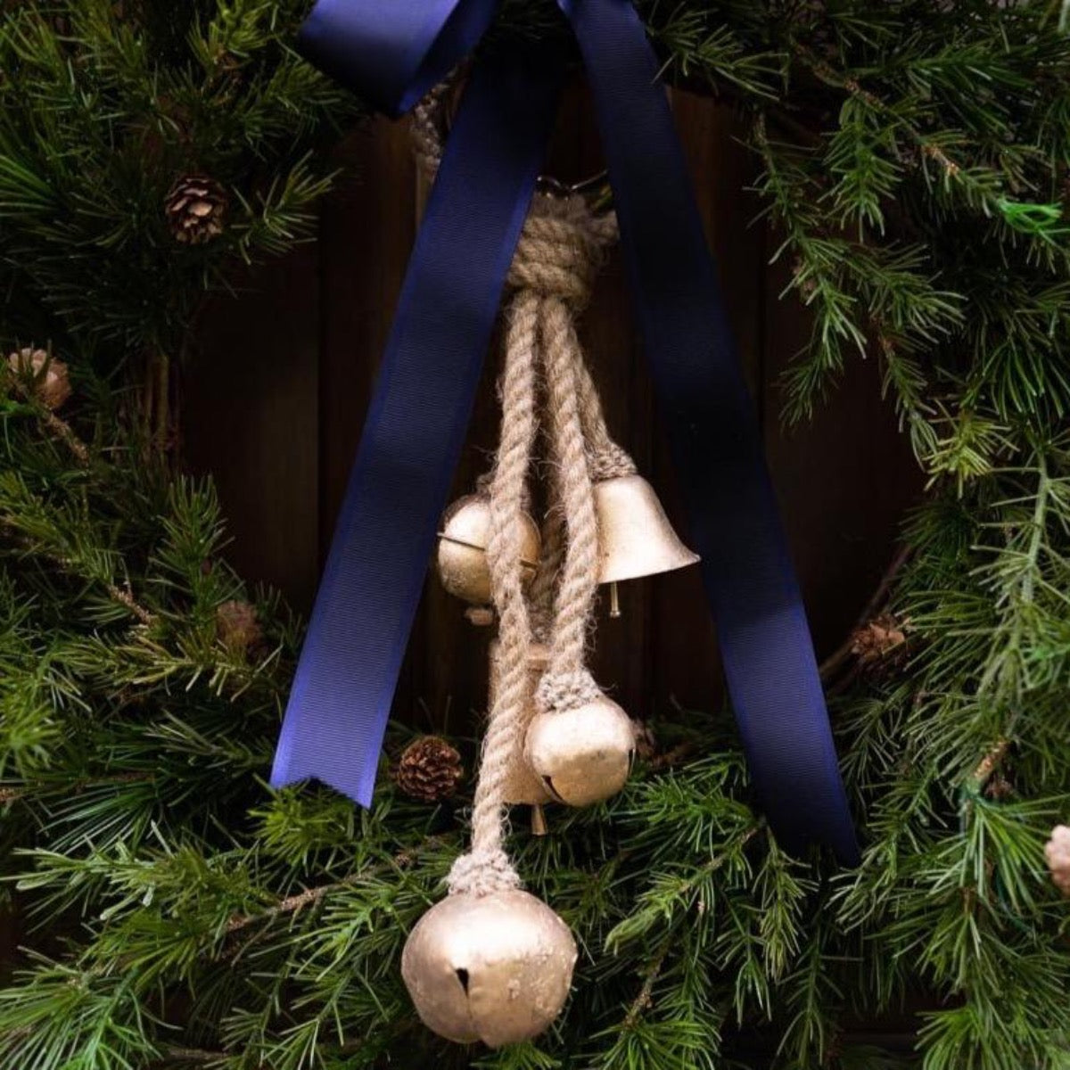 Jute Metal Bells hanging on a wooden door with greenery. Styled view.