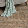 Jute Woven Seaglass Rug styled under a grey chair with blue throw. Styled view.