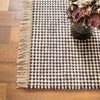 Kuba Black Woven Jute Rug styled on a wood floor with florals. Styled view. 