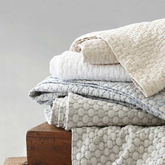Folded stack of coverlets in multiple colours. Styled view.