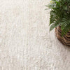 Niels Ivory Woven Wool/Viscose Rug styled under a woven planter. Styled view. 