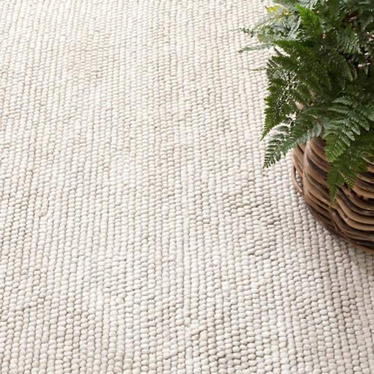 Niels Ivory Woven Wool/Viscose Rug styled under a woven planter. Styled view. 