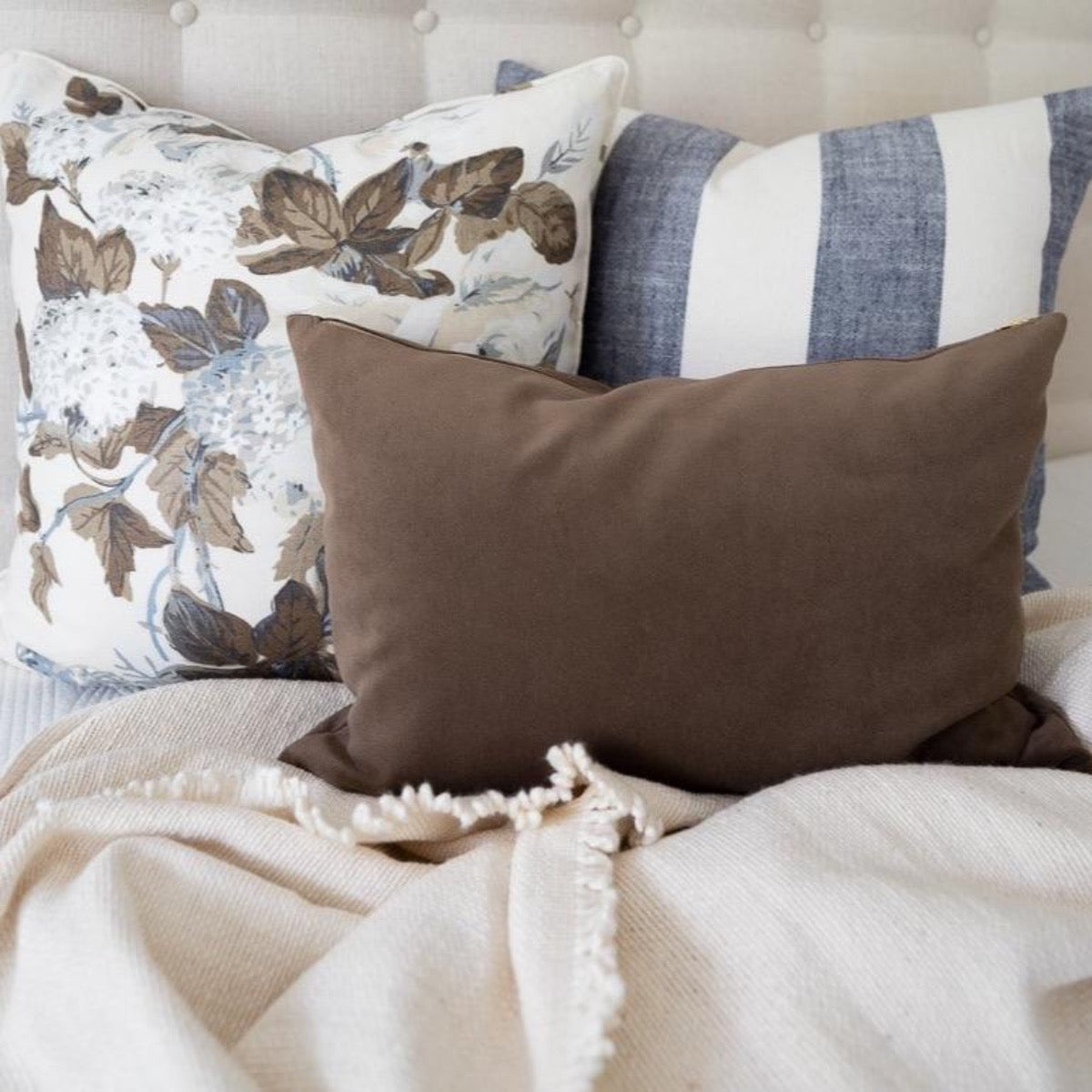 Royal Velvet Lumbar Pillow - Cocoa styled with brown and navy pillows on a neutral bed. Styled view. 
