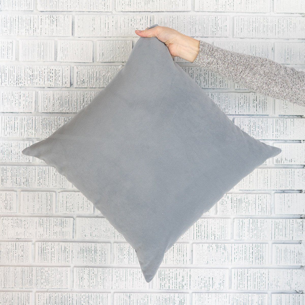 Royal Velvet Pillow - Dove Grey against a white brick wall. Styled view. 