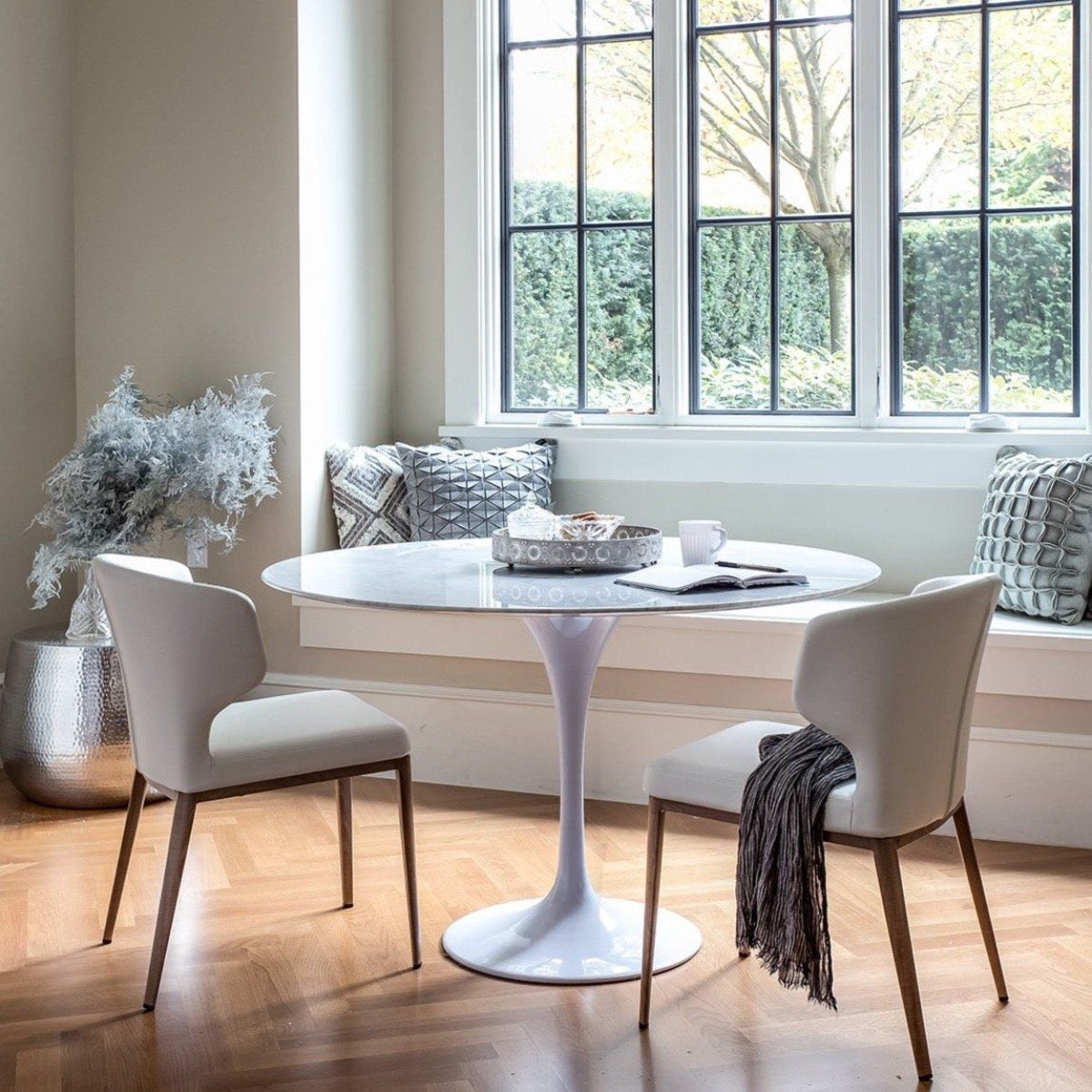 Trumpet Dining Table Round - Condo Size styled with white chairs and a bench. Styled view. 