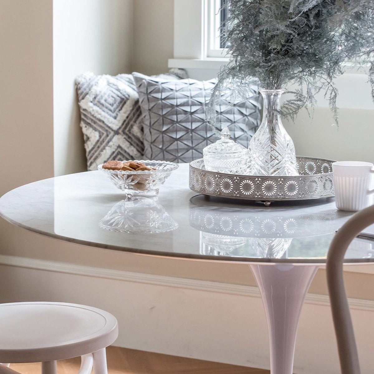 Trumpet Dining Table Round - Condo Size styled with serveware and greenery with decorative pillows. Styled view.