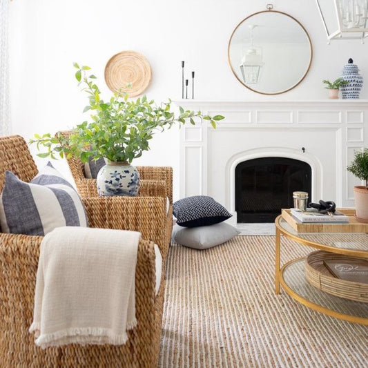 Twiggy Natural Woven Wool/Jute Rug styled in a white living room with wicker chairs and white mantel. Styled view. 