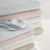 Folded stack of washed linen bedding in multiple colours. Styled view.